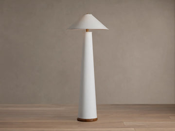 Ombra Floor Lamp: a tall white conical lamp with a white linen shade, teak base, and antiqued brass accents, on a wooden floor.