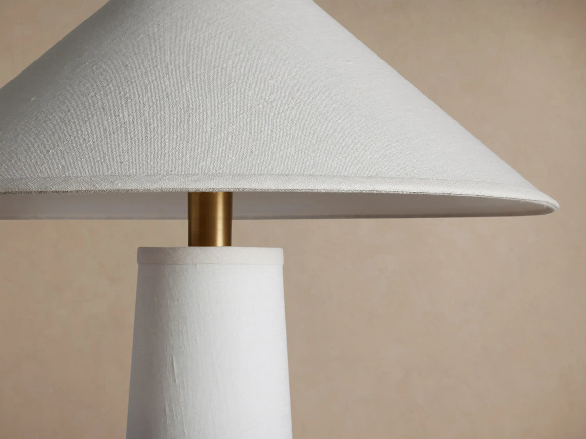 Ombra Floor Lamp with a white tapered body, light linen conical shade, and a round teak wood base, accented with antiqued brass.