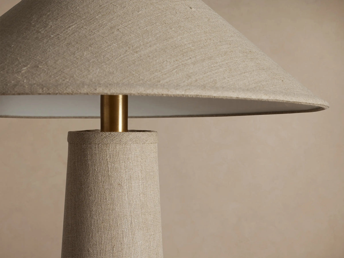 Ombra Floor Lamp, beige linen tapered column & conical shade, antiqued brass accent, teak wood base, on wood floor.