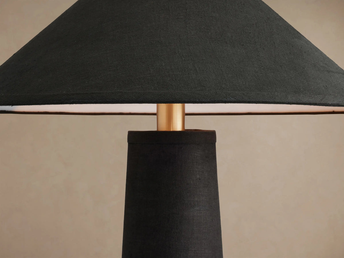 Ombra Floor Lamp, standing upright. Features a black conical linen shade and base, with antiqued brass and teak wood accents.