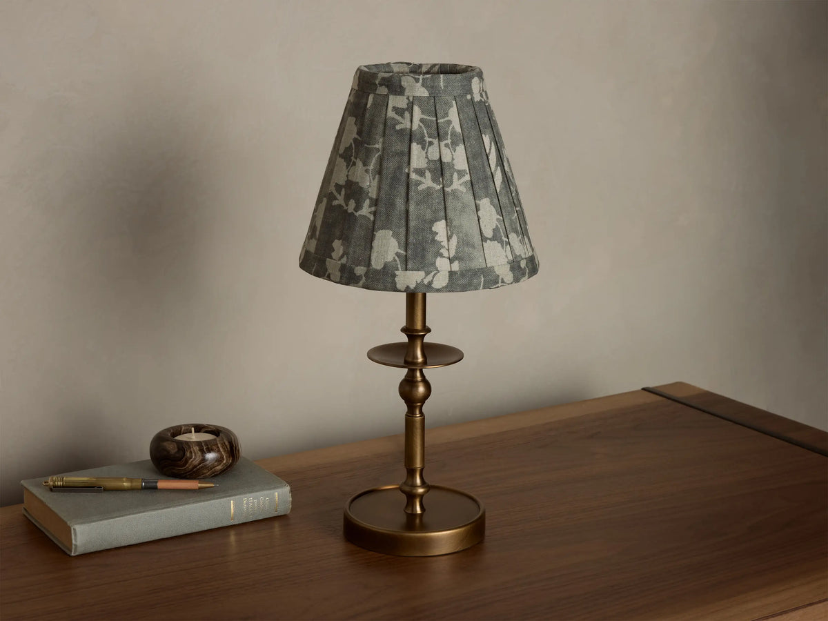 Front view of the Winslow Accent Table Lamp with an antique brass base and a pleated grey fabric shade with white floral pattern.