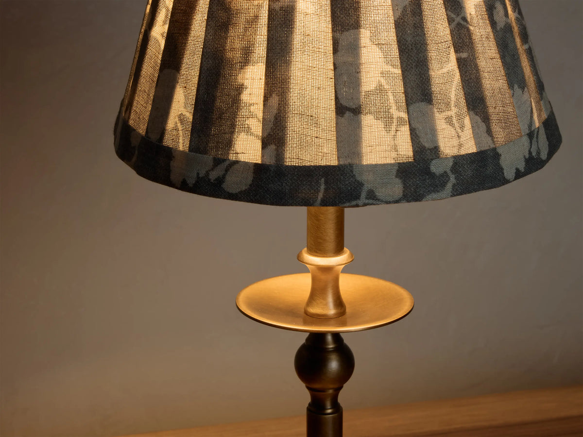 Front view of the lit Winslow Accent Table Lamp, featuring an antique brass finish base and a pleated dark floral fabric shade.