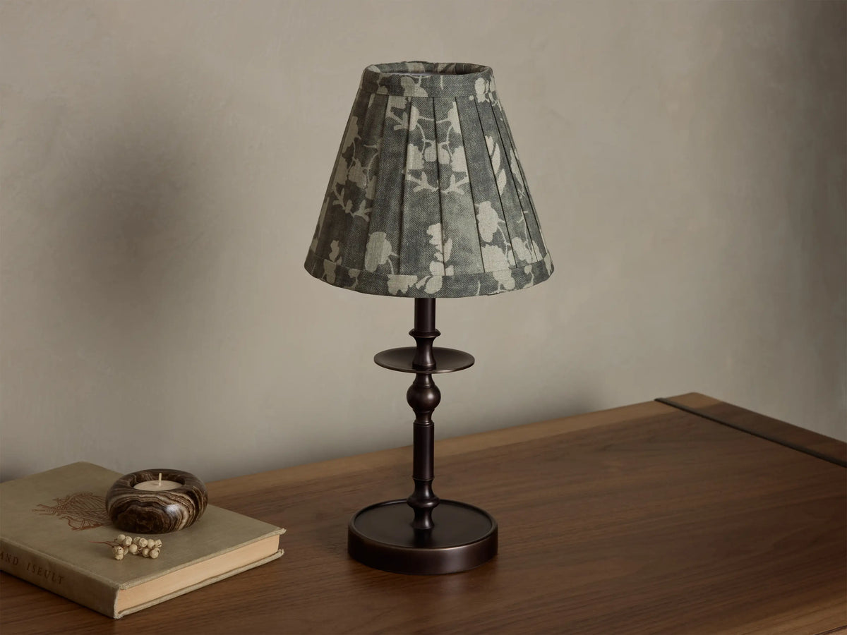 Bronze Winslow Accent Table Lamp with a pleated dark patterned fabric shade, illuminated, casting a warm glow on a wooden table.