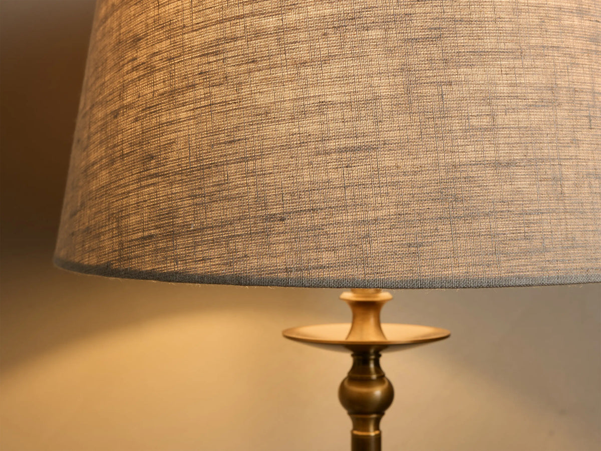 Close-up of the Winslow Table Lamp, showing warm light from its charcoal fabric shade with visible weave, and antique brass base.