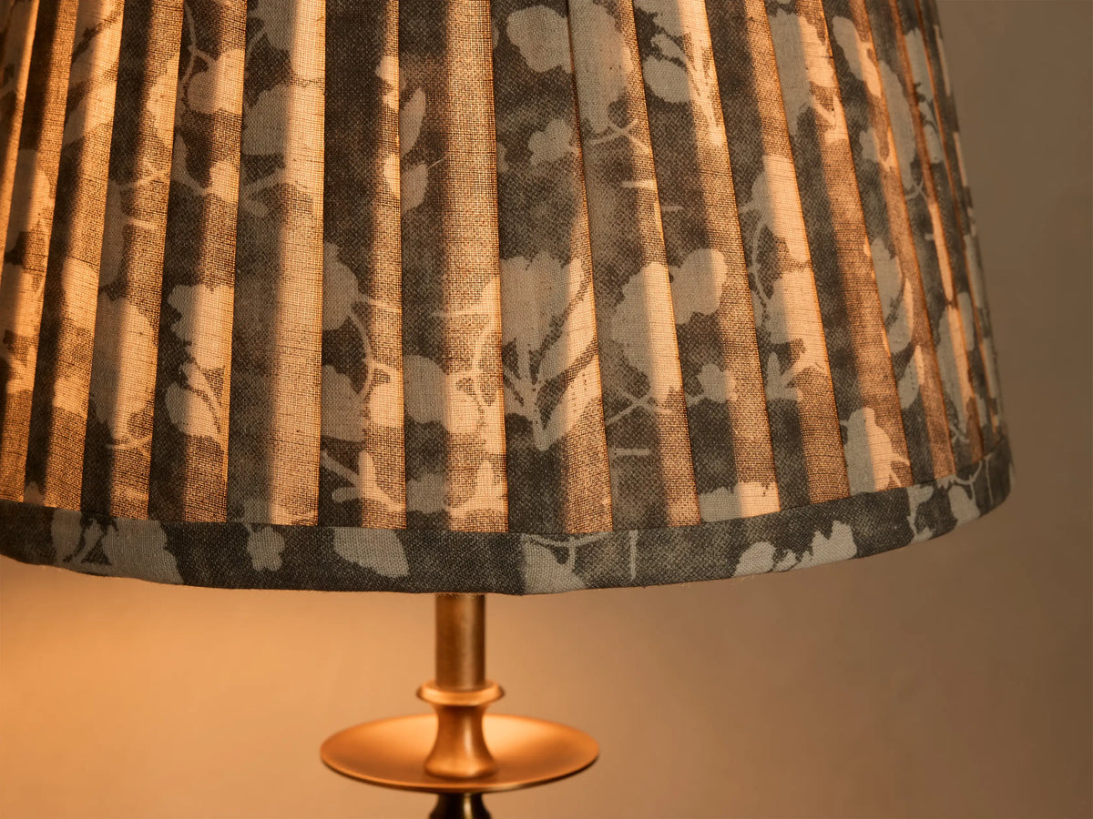 Close-up of the pleated fabric shade on a Winslow Table Lamp, featuring a gray floral pattern and warm light on an antique brass base.