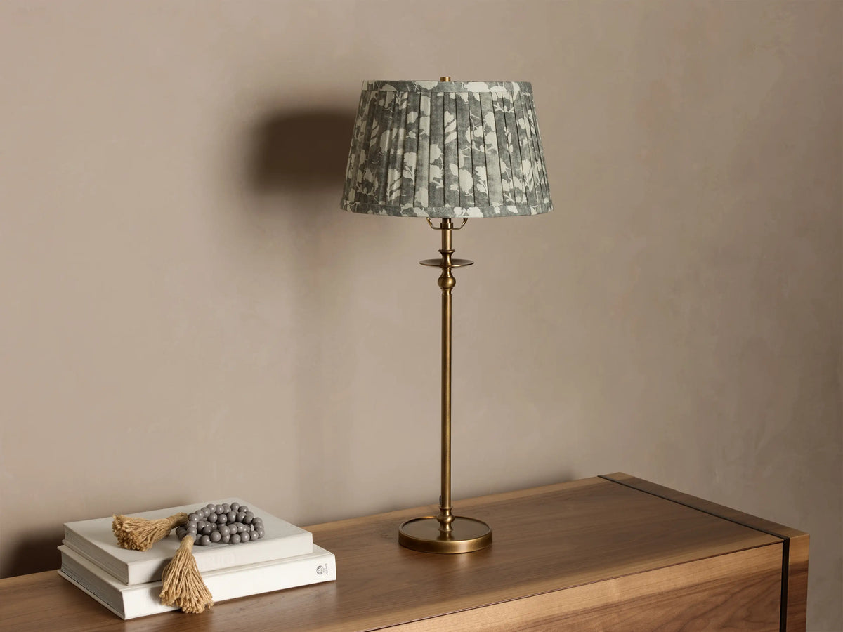 Winslow Table Lamp with an antique brass base and a pleated greenish-gray floral fabric shade on a wooden surface.