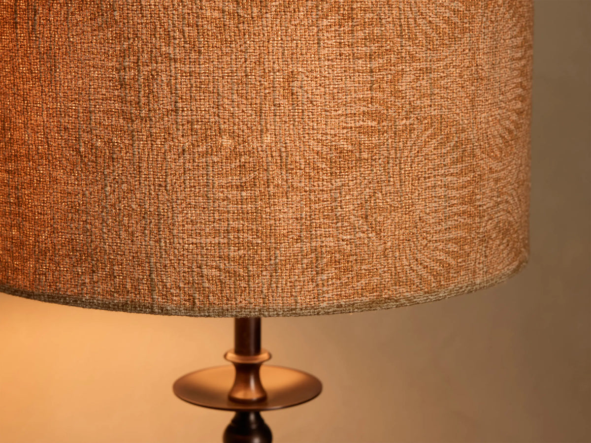 Close-up of the illuminated Winslow Table Lamp's textured orange-tan fabric shade with a subtle pattern, and dark bronze metal base.