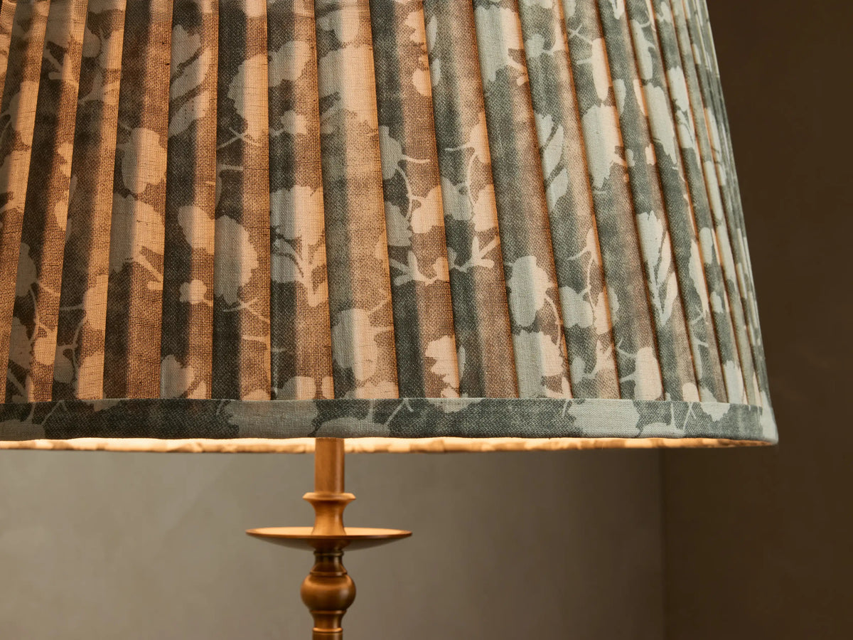 Front view of the antique brass Winslow Floor Lamp with a pleated fabric shade, casting a warm glow on a wall.