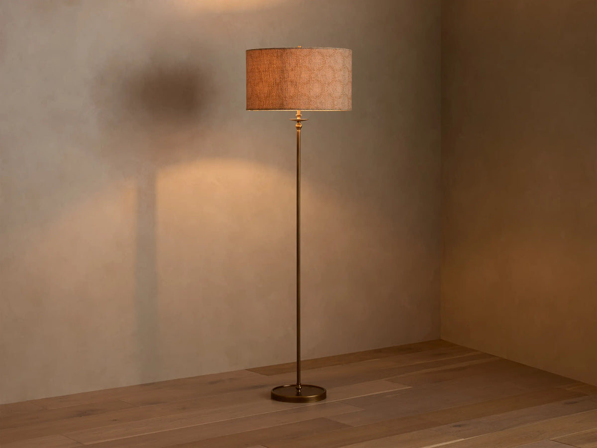 Full view of the Winslow Floor Lamp with antique brass finish and a textured light brown fabric shade, illuminating a room corner.