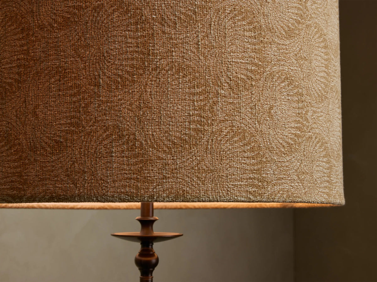 Close-up of the Winslow Floor Lamp. Textured brown/tan fabric shade, subtle pattern, antique brass base. Illuminated from below.