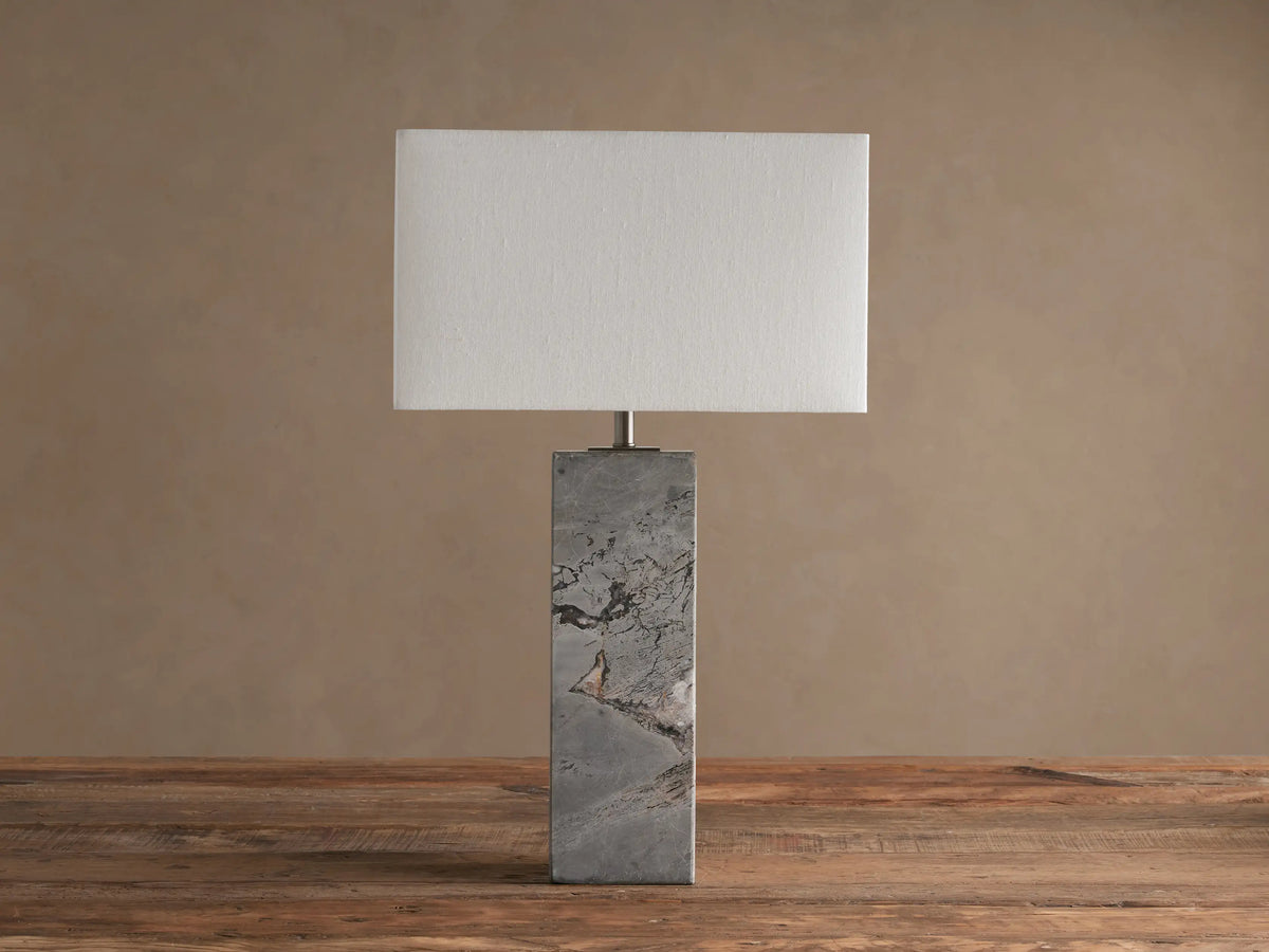 Oren Table Lamp with rectangular white linen shade and gray natural stone base with veining, on a rustic wooden table.