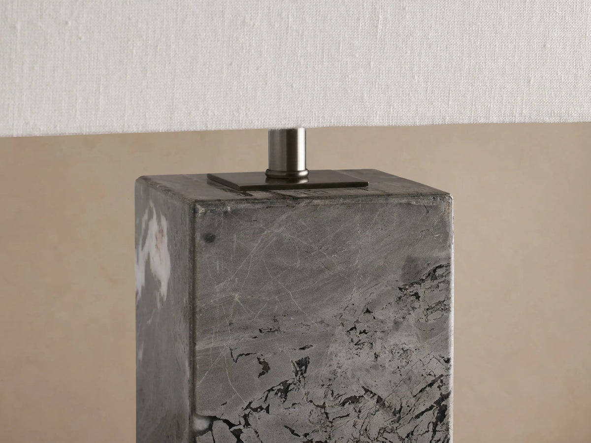Close-up of Oren Table Lamp. Rectangular gray stone base with dark veining supports a white linen shade on a silver metal rod.