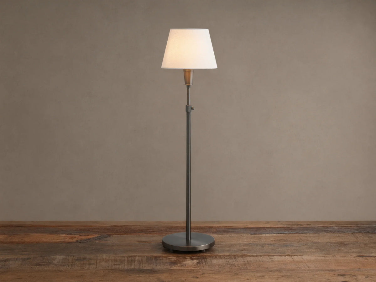 Upright pewter Candice Table Lamp with a creamy white conical shade, standing on a distressed wooden table against a warm neutral wall.