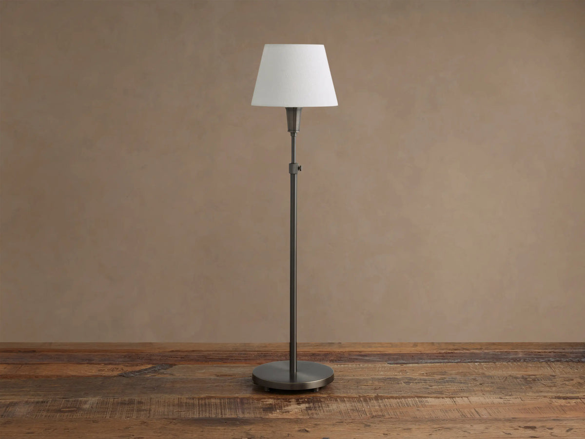 Upright pewter Candice Table Lamp with a creamy white conical shade, standing on a distressed wooden table against a warm neutral wall.