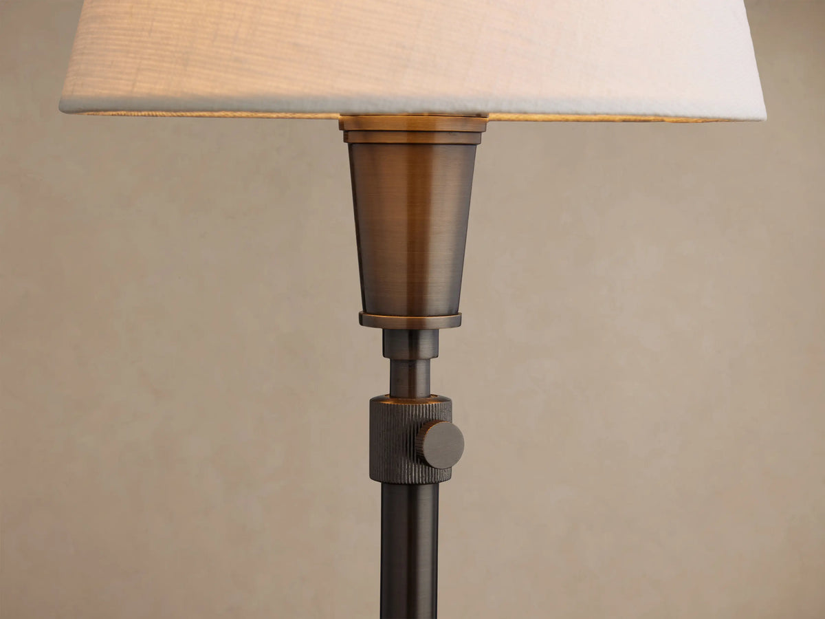 Candice Table Lamp in Pewter with a white conical shade, standing on a rustic wooden table against a brown wall.