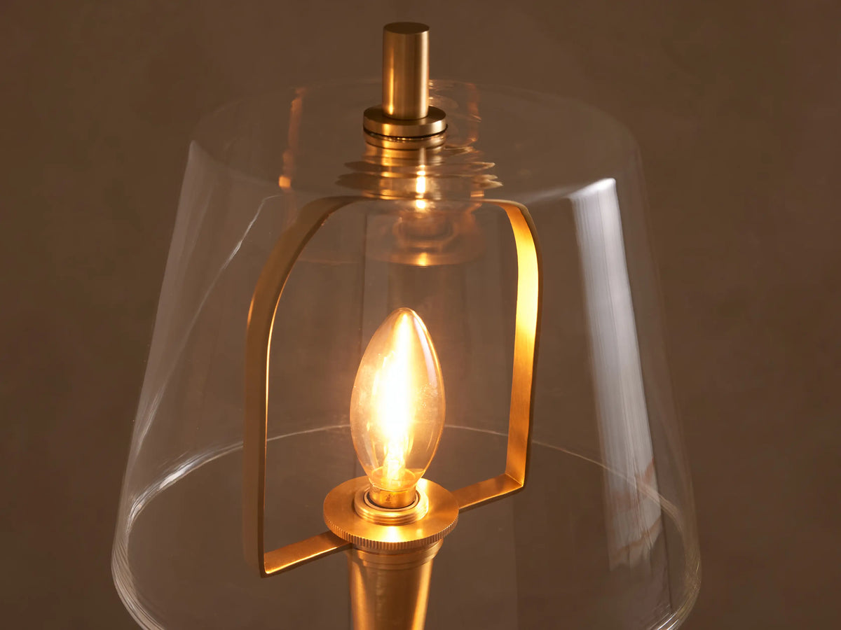 Candice Floor Lamp with a slender brass finish and clear glass shade, standing on a wooden floor against a neutral wall.