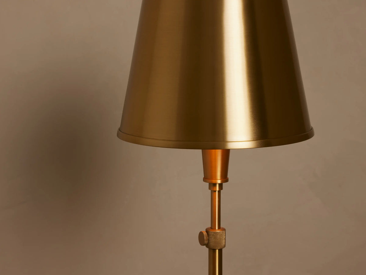 Candice Floor Lamp, brass finish, with a matching brass conical shade, standing upright in a room corner with wood floor.