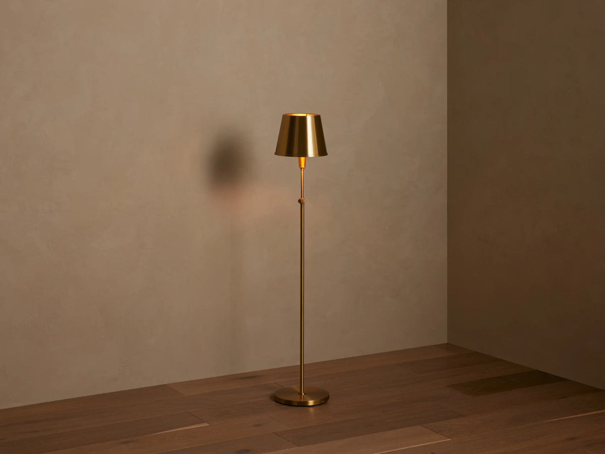 Partial view of Candice Floor Lamp; metallic brass conical shade and stem with a knurled switch, casting a warm glow.