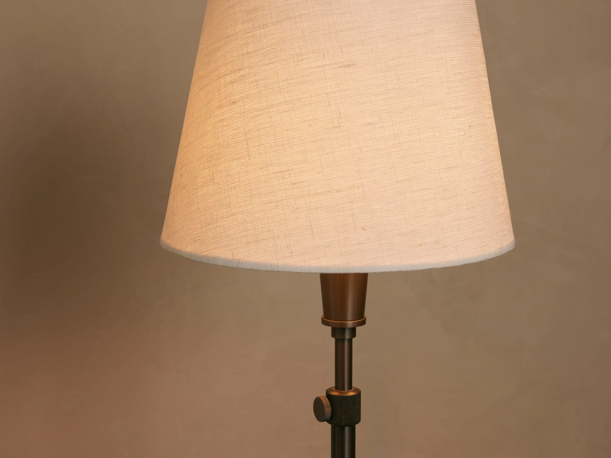 Candice Floor Lamp, black iron with white conical shade, centered on a wooden floor against a beige wall.