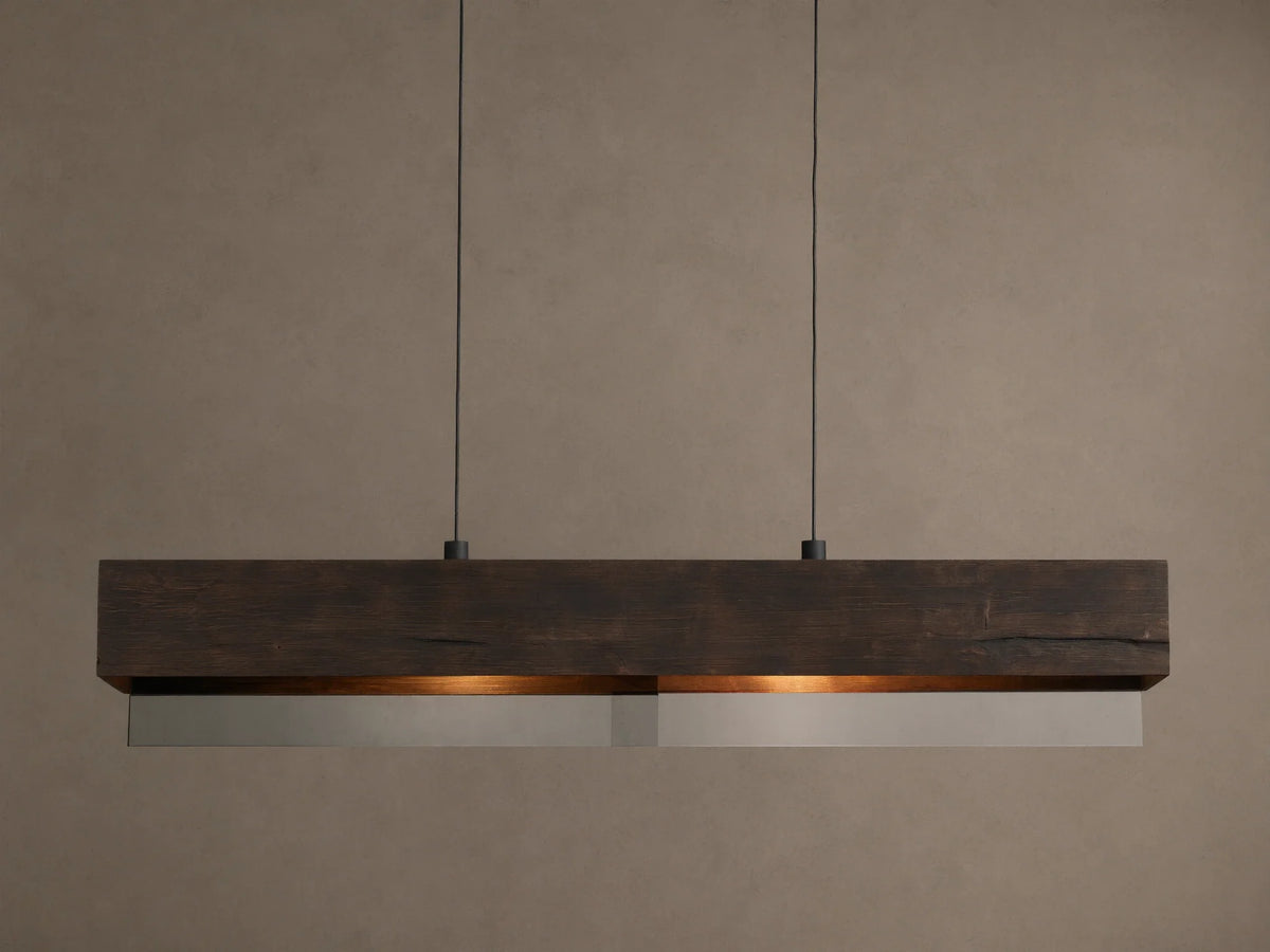 Lena Linear Chandelier: A rectangular dark wood beam with textured grain, featuring mirrored glass below, emitting a warm glow, suspended by black cords.