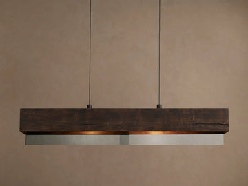 Lena Linear Chandelier: a dark alder wood beam with ochre finish and mirrored glass bottom, emitting warm light, suspended by two black cords.