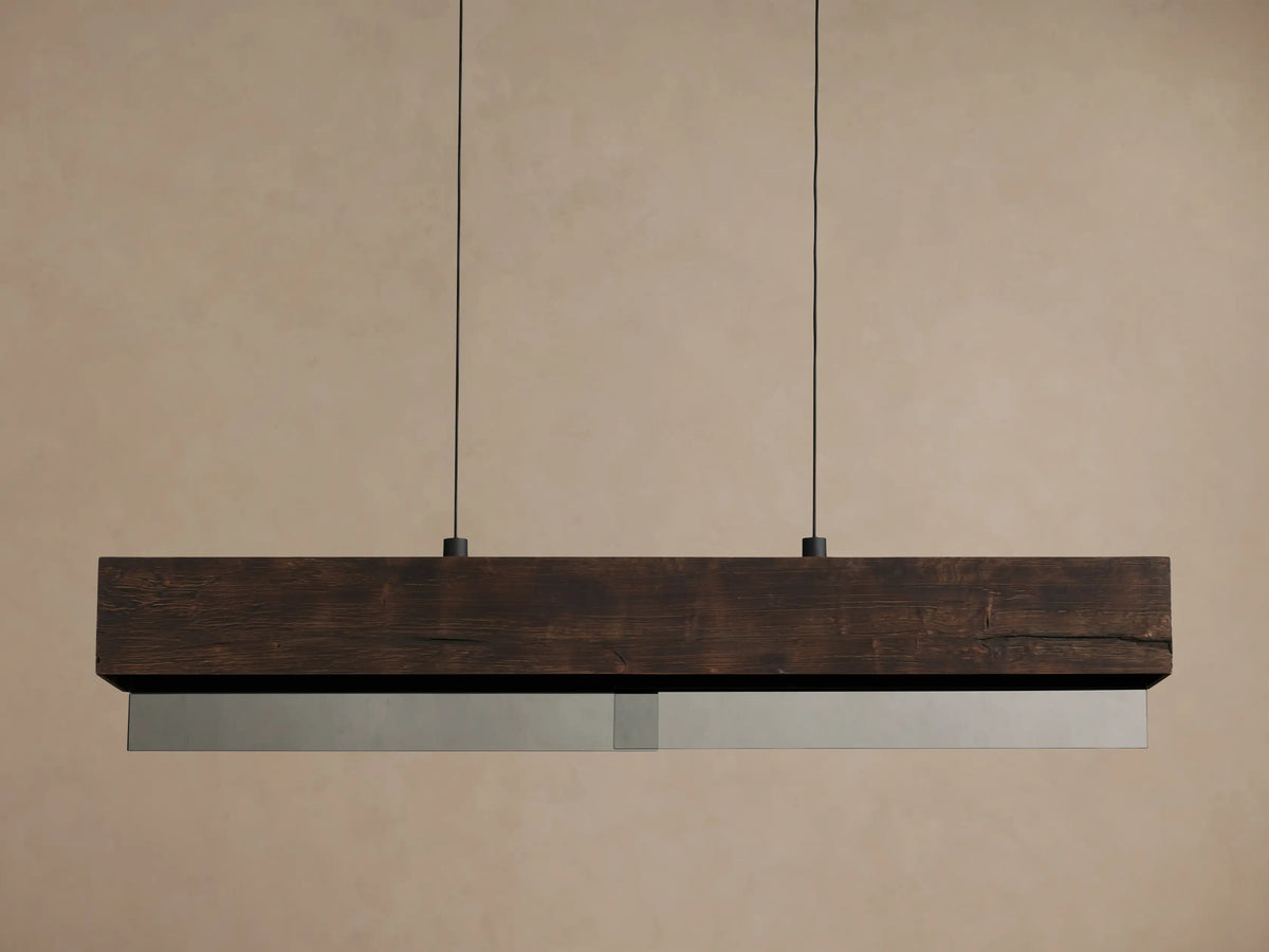 Lena Linear Chandelier: a dark alder wood beam with ochre finish and mirrored glass bottom, emitting warm light, suspended by two black cords.