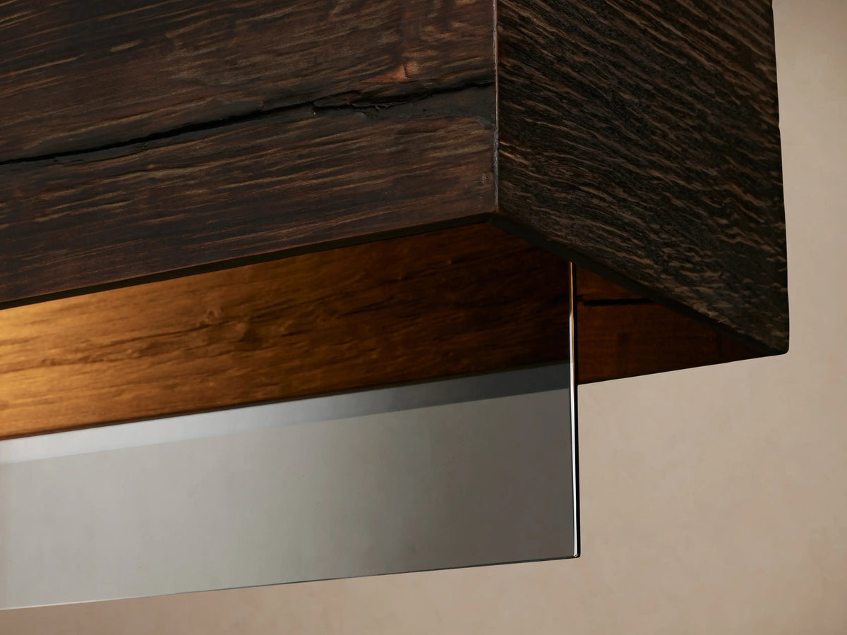 Lena Linear Chandelier: dark ochre alder wood beam and mirrored glass panel, hanging from black cords against a beige wall.