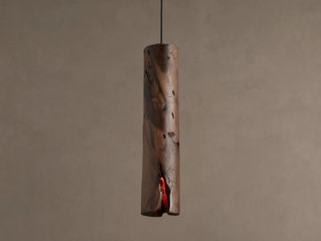 Dedalo Pendant, a cylindrical milpa wood light with natural texture, hangs vertically. An orange glow emanates from a front crack.