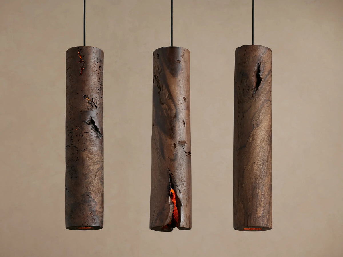 Dedalo Pendant, a dark milpa wood cylinder with a natural, deep vertical crack glowing warm orange from within, against a light wall.