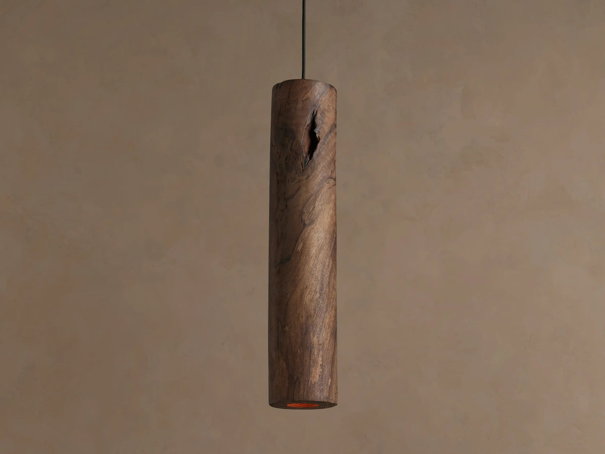 Dedalo Pendant: Rustic dark brown cylindrical wood pendant with natural knots & grain, hanging vertically on a beige wall.