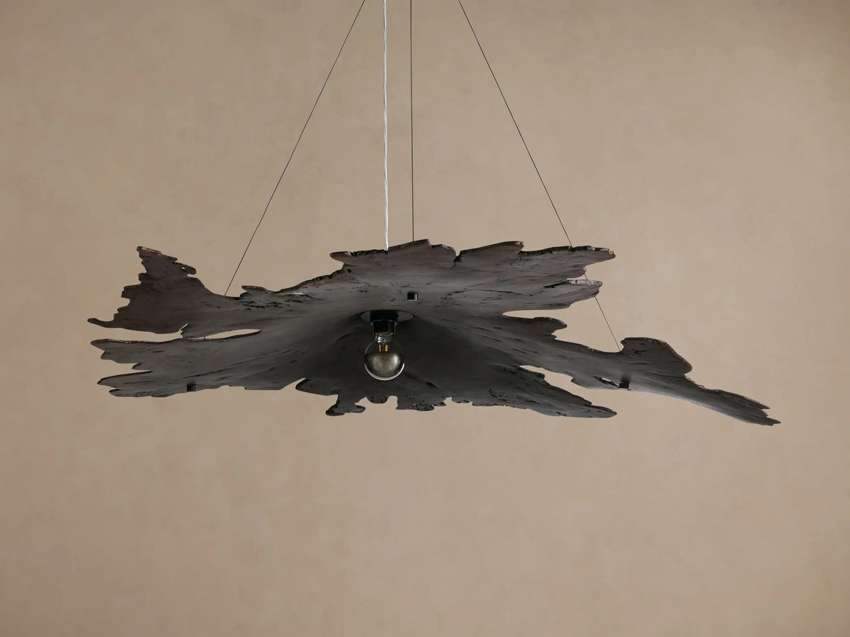 Arruga Chandelier: dark, irregular milpa wood chandelier with an exposed bulb hanging from a ceiling against a warm background.