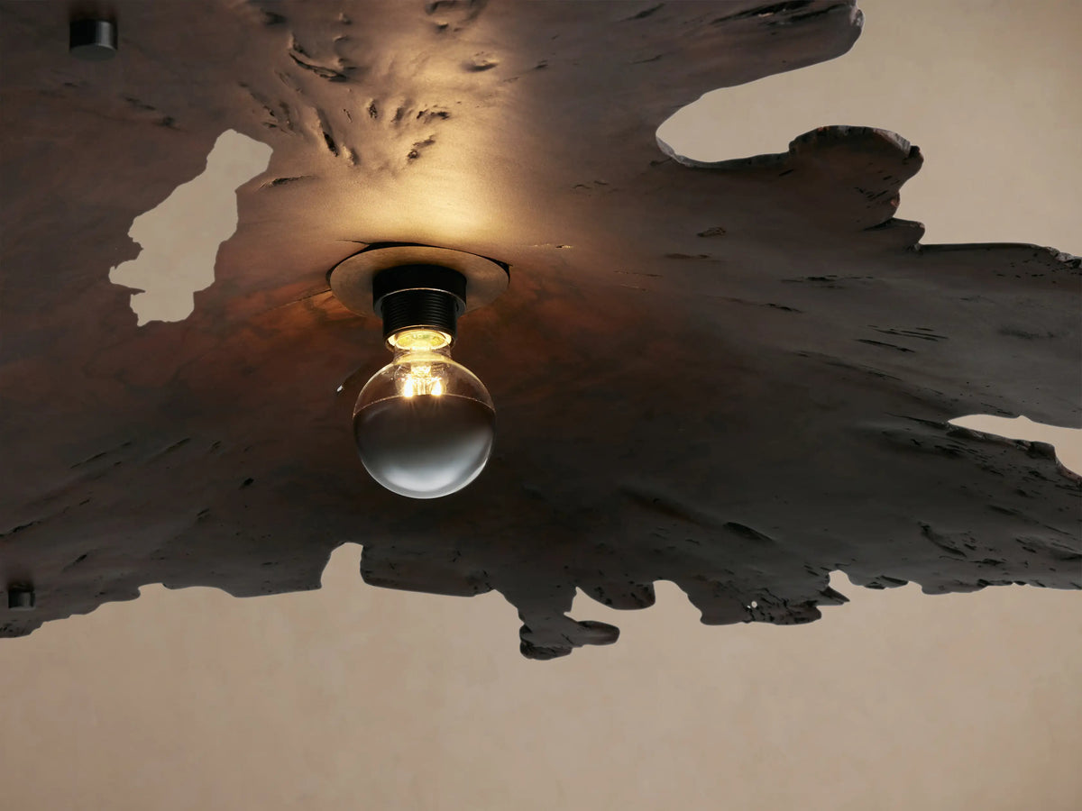 Arruga Chandelier: Dark, naturally shaped milpa wood with irregular, jagged edges, a bulb centrally underneath, suspended from cables.
