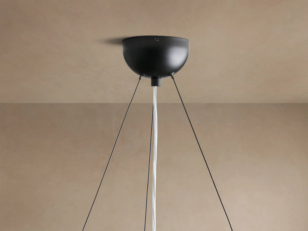 Close-up of Arruga Chandelier; a clear, glowing bulb illuminates the dark, textured, irregularly shaped milpa wood dome from below.