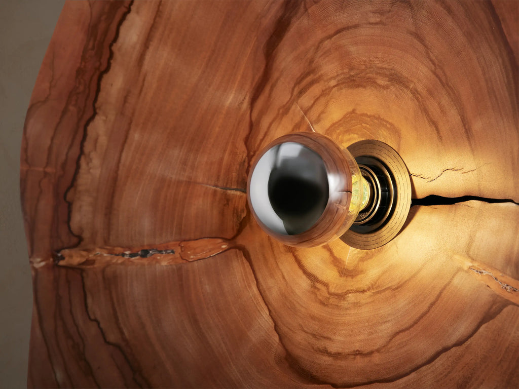 Arruga Sconce: Dome-shaped milpa wood sconce with rich brown grain, cracks, and a metallic bulb in the center, on a beige wall.