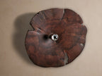 Arruga Sconce: Domed, irregular dark milpa wood sconce with natural grain & cracks, a silver bulb glowing from its center on a wall.
