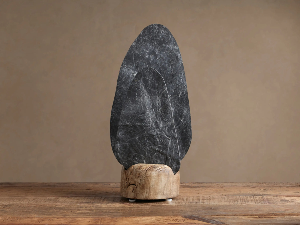 Shinto Table Lamp. Two irregular slate stone shades, dark gray front, lighter illuminated rear, in a natural wood base on a wood table.