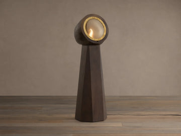 Agustin Floor Lamp: Dark wood faceted base with a round, gold-rimmed opaque glass light fixture, glowing warmly.