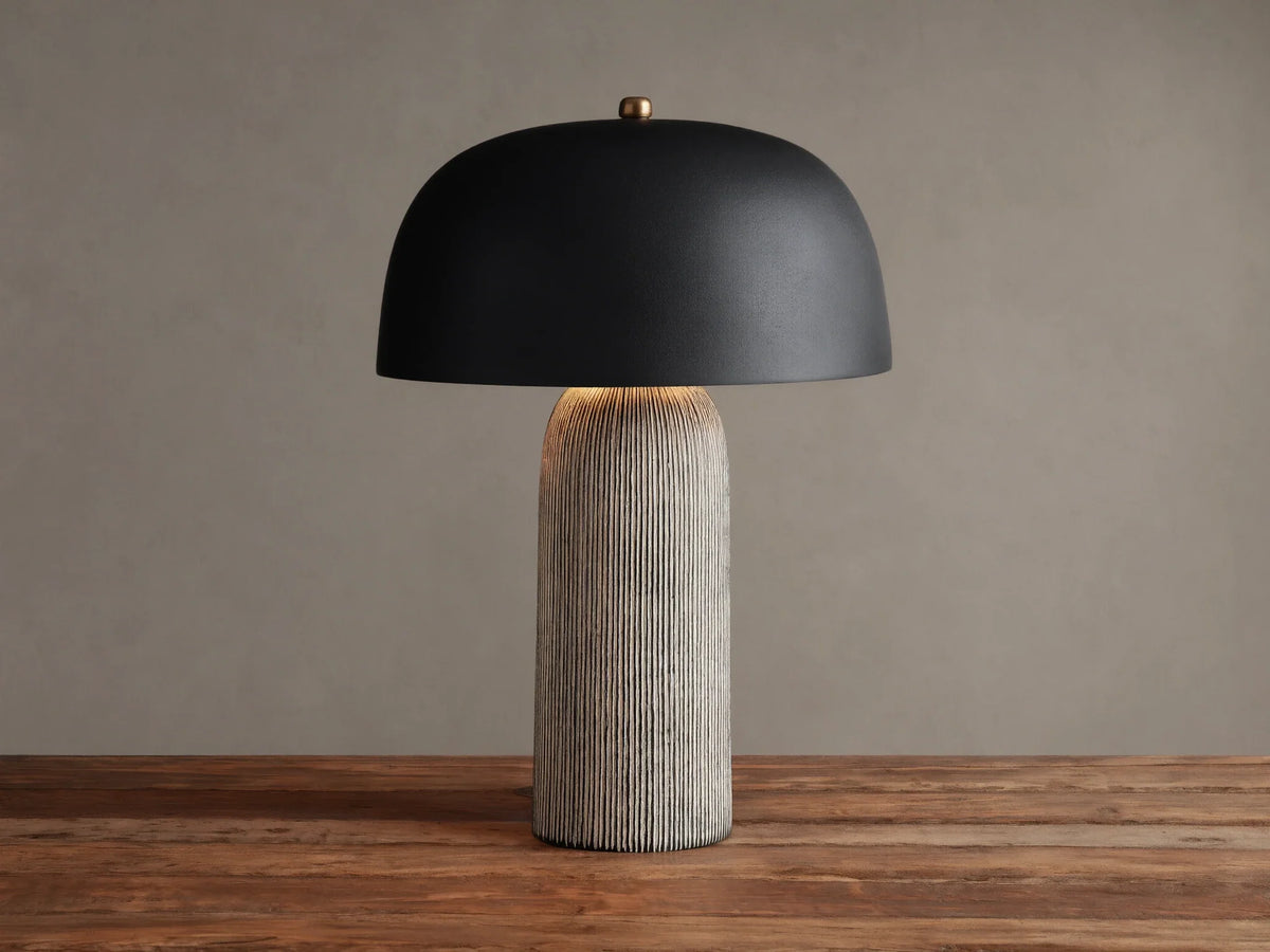 Ira Striped Table Lamp with black dome shade, light-colored vertically ribbed base, on wood table, softly lit.