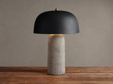 Ira Striped Table Lamp with black dome shade, light-colored vertically ribbed base, on wood table, softly lit.