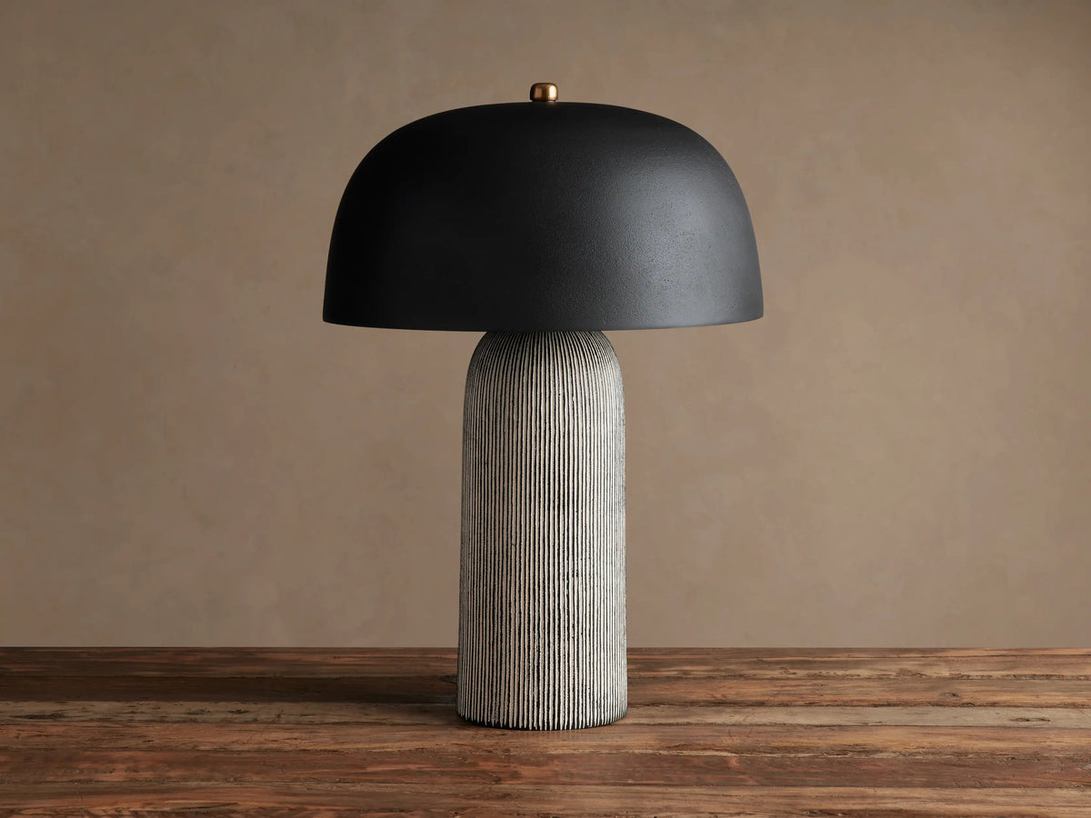 Ira Striped Table Lamp with black dome shade, light-colored vertically ribbed base, on wood table, softly lit.