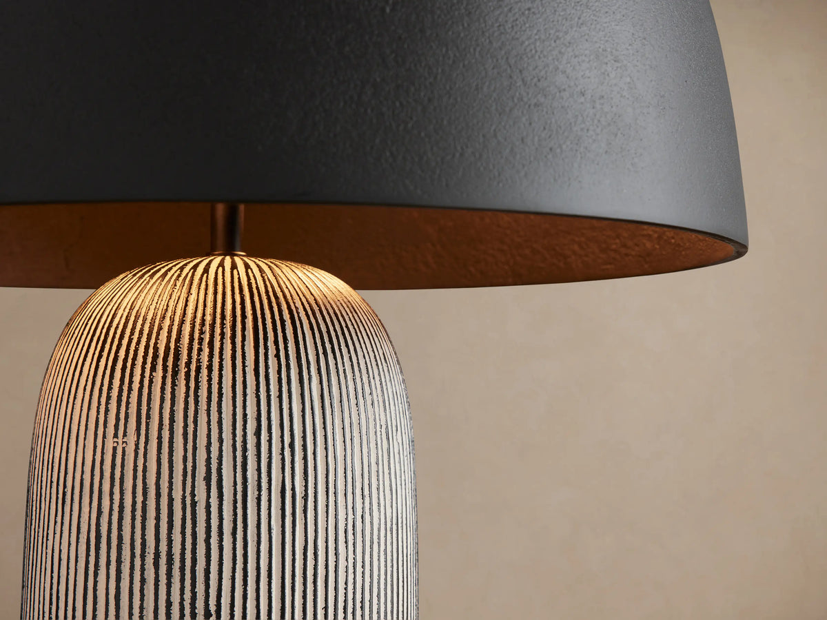 Ira Striped Table Lamp with black dome shade, textured gray striped cylindrical base, and small gold knob, on wooden table.