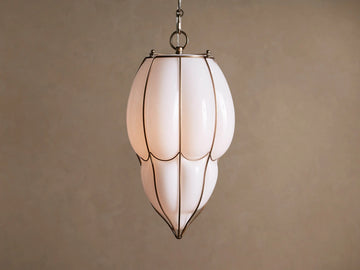 Margolis Large Pendant: Elongated white opaque glass pendant light with brass-finished frame, glowing softly, against a neutral wall.
