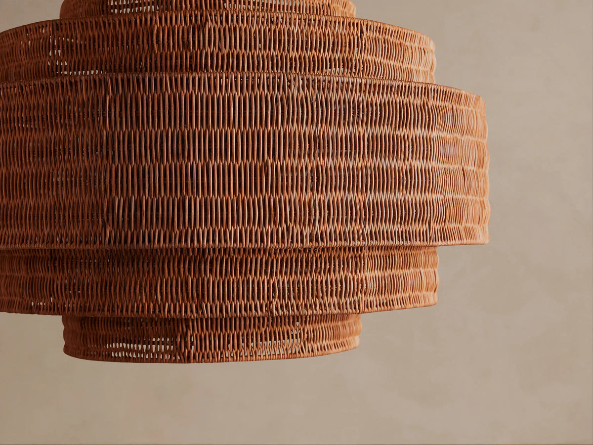 Paloma Chandelier: Tiered handwoven warm brown rattan shade, suspended from a metal chain against a neutral background.