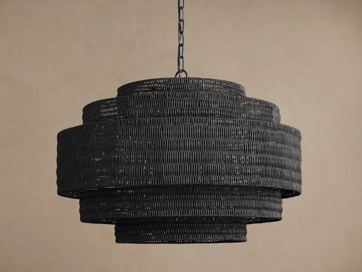 Paloma Chandelier, dark grey handwoven rattan with three concentric tiered shades, suspended by a black chain. Warm glow from within.