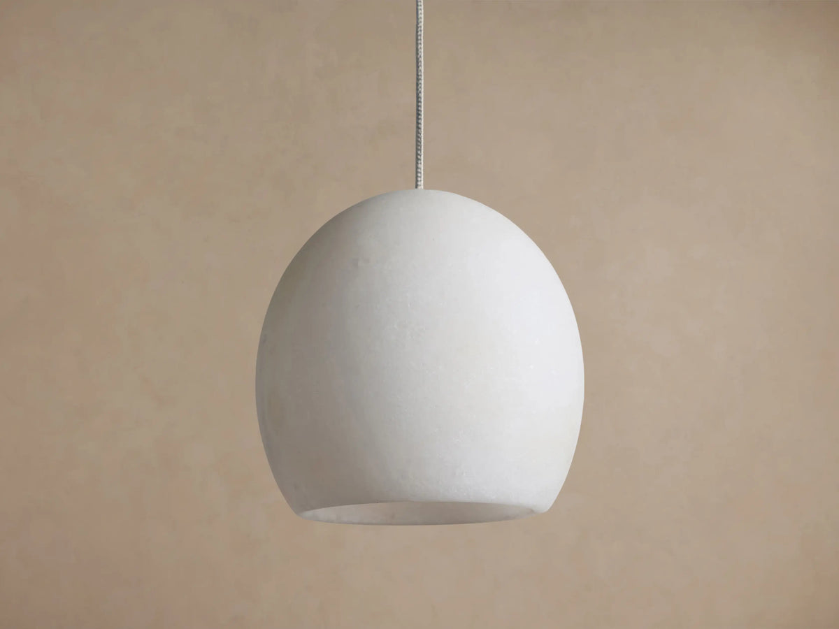 Arica Pendant with a spherical, light cream alabaster shade suspended from a thin cable, emitting a soft glow.