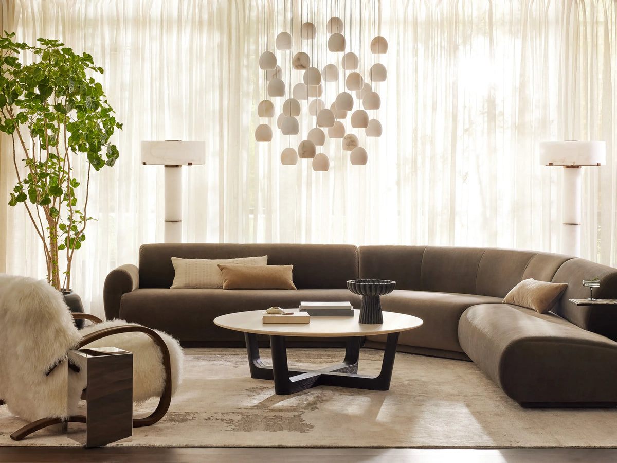 Arica Round Chandelier: 7 illuminated, spherical alabaster shades suspended at varying heights on thin cables against a brown wall.