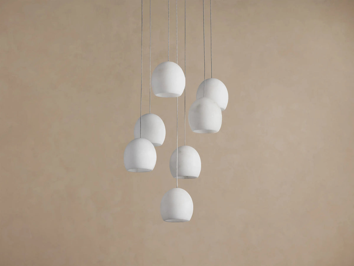Arica Round Chandelier with multiple white spherical alabaster shades hanging from thin cables against a beige wall.
