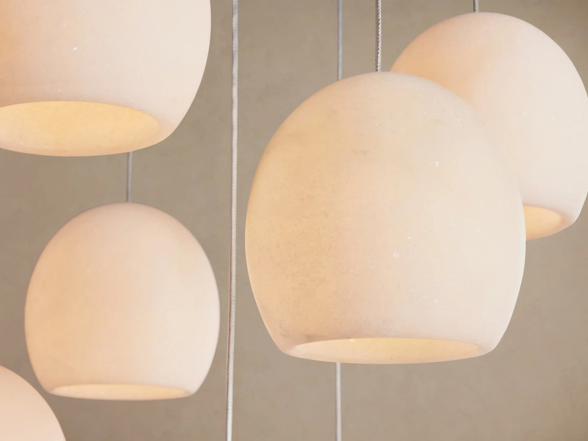 Arica Round Chandelier close-up: several glowing, off-white spherical alabaster shades hanging on cables.