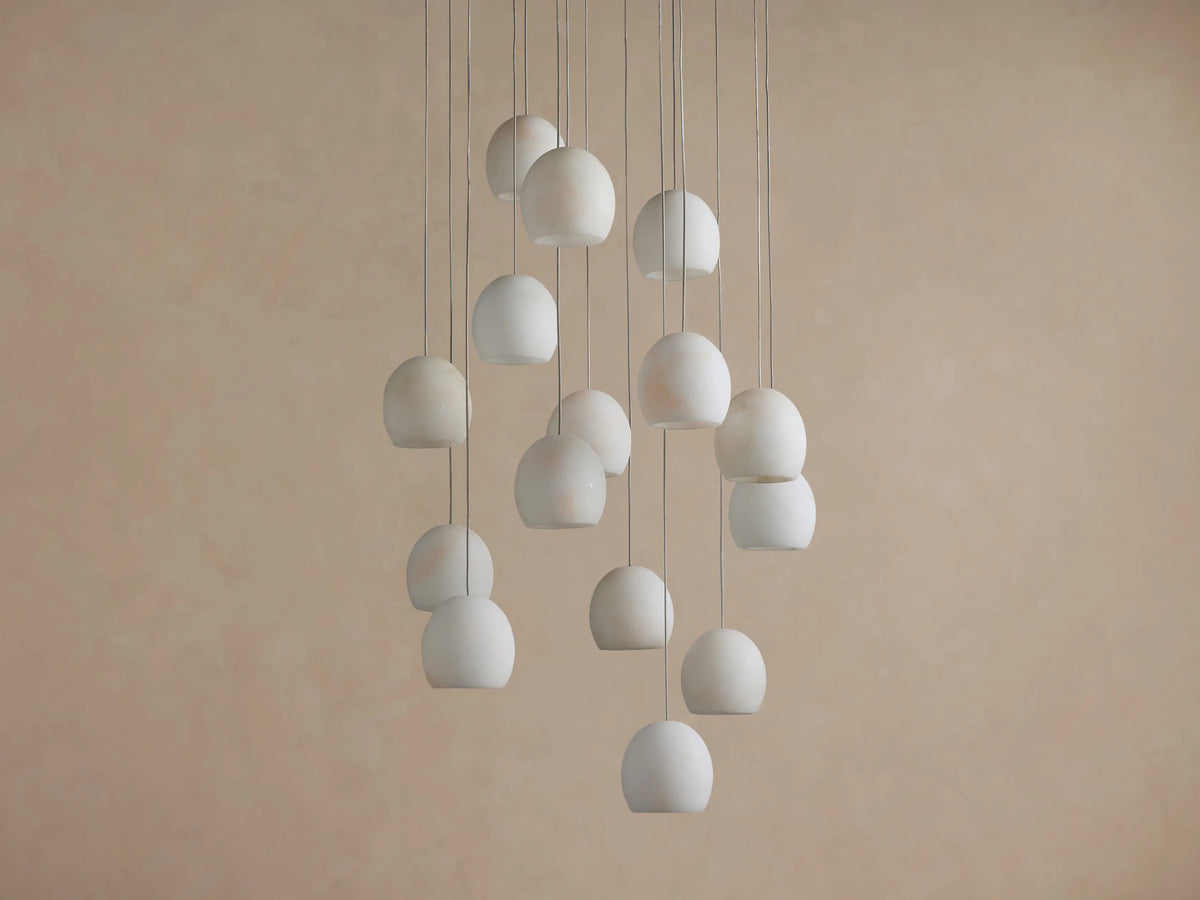 Arica Round Chandelier: Multiple round, illuminated alabaster shades hanging at different heights against a warm beige wall.