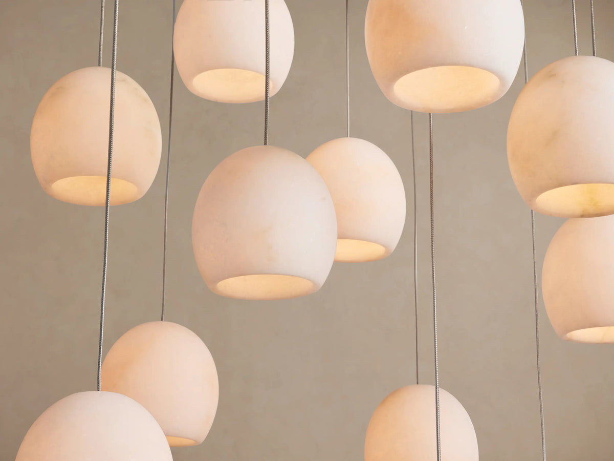 Multiple pale alabaster stone globe shades of the Arica Round Chandelier glow softly, suspended by thin cables.